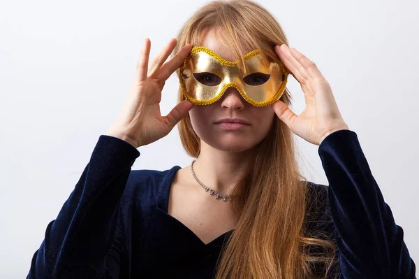 young woman with ginger hair and freckles dressed in dark velvet dress wearing golden mask on party