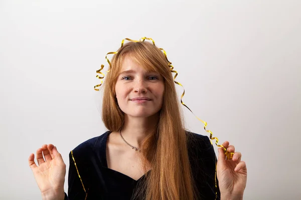 young woman with ginger hair and freckles dressed in dark velvet dress playing with golden party garland