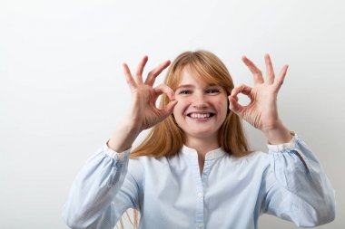 Kızıl saçlı kadın çiller ile onayı ile parmak belirtileri gösteriyor ve mutlu bir şekilde gülümseyerek rahat mavi gömlek giymiş 