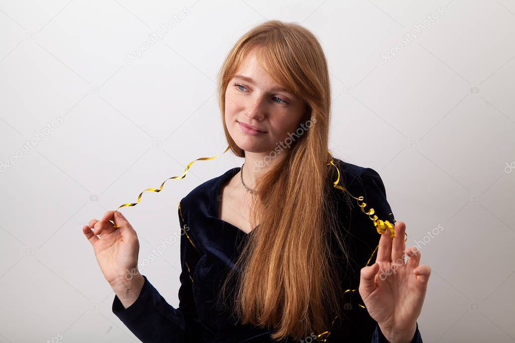 attractive woman with ginger hair and freckles dressed in dark velvet dress playing with golden party garland and looking aside with soft smile 