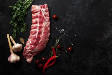 pişmemiş Domuz kaburga kiraz domates ve biber otlar ve karanlık dokulu arka plan, akşam yemeği malzemeler kavramı üzerine sarımsak ile 