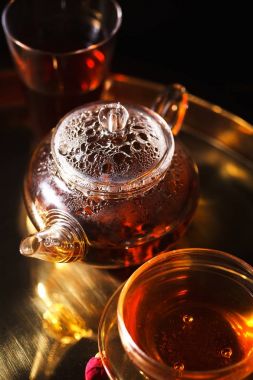 küçük cam çaydanlık ve bardak sıcak kırmızı çay ve altın tepsi, kurutulmuş gül yaprakları ile dikey yakın çekim çekim altın renk kavramı