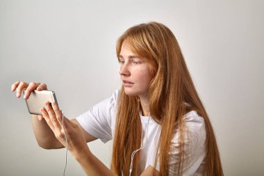 Kızıl saçlı olan kadın çiller ile yatay pozisyonda tutan telefon kulaklık takılı 