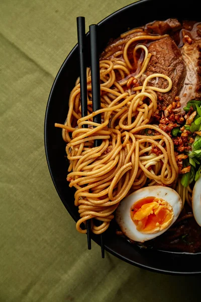 bowl with japanese ramen with pork belly and mushrooms with marinated eggs on green linen tablecloth