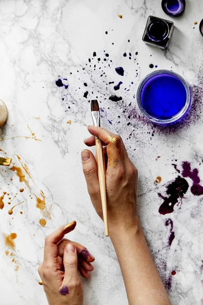 view of female artist hands soiled with golden and violet paints on white background, artist workspace concept