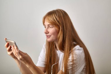 Kızıl saçlı olan kadın çiller ile yatay pozisyonda tutan telefon kulaklık takılı 