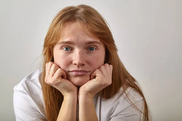 young woman with red hair and freckles dressed in boyfriend-styled white t-shirt feeling bored and looking at the camera