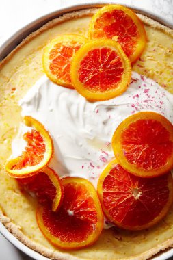 Cheesecake karamelize kırmızı portakal ve beyaz mermer masada krem şanti ile