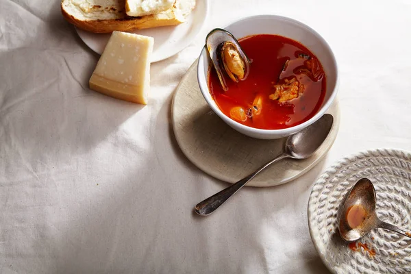 Traditional mediterranean soup bouillabaisse with mussels and shrimps with tomatoes and fish broth served in white bowl with warm baguette and cheese on plate , Holiday meal concept — Stock Image Traditional Mediterranean Soup Bouillabaisse Mussels Shrimps Tomatoes Fish Broth Served Stock Photo