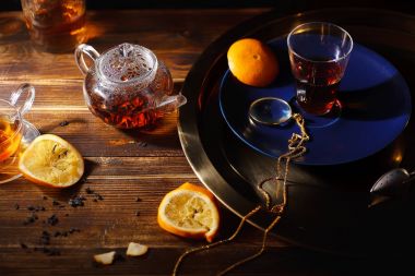 sıcak siyah çay çaydanlık ve Kupası ile cep Büyüteç ahşap zemin üzerine altın tepsi  