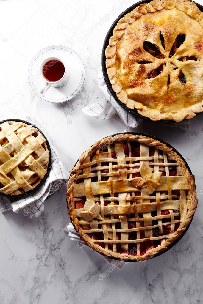 apple with strawberry and raspberry cooked pies with lattice and leaves and tea on white marble table 