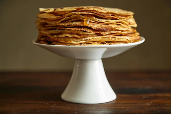 white cake stand with crepes cake and orange jam with honey on wooden table, close-up