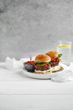 Beyaz seramik plaka Burger ve sos bardak limonlu su üzerinde ahşap masa, kase ile yakın çekim 