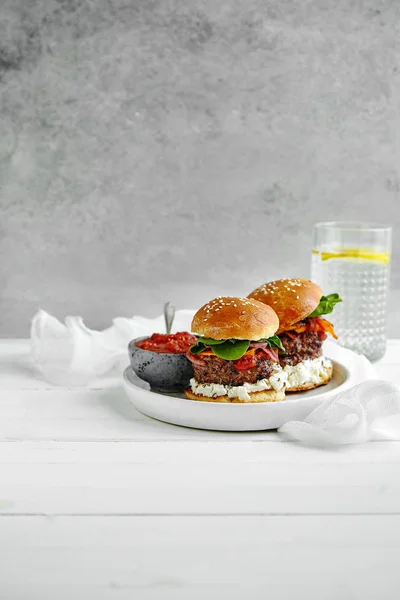 white ceramic plate with burgers and sauce in bowl with glass of lemon water on wooden table, close-up