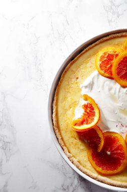 Cheesecake karamelize kırmızı portakal ve beyaz mermer masada krem şanti ile