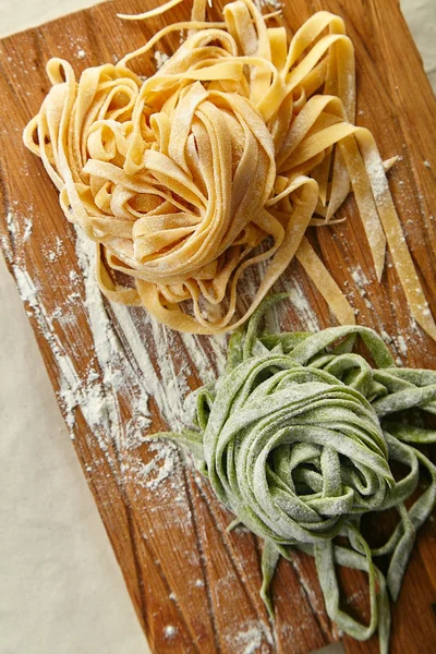 two types of handmade italian tagliatelle pasta on wooden cutting board