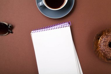 defter ile çikolatalı çörek ve bununla birlikte güneş gözlüklü kahverengi zemin üzerine siyah kahve 