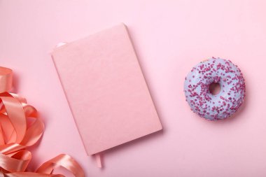 pembe defter ile parlak pembe saten kurdele ve pembe arka plan tek renk kavramı üzerinde tatlı çörek 