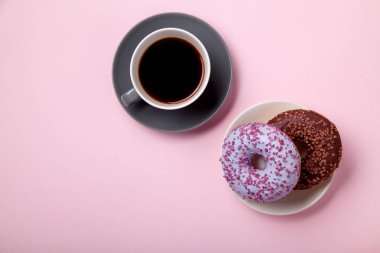 Çikolatalı donuts pembe arka plan üzerinde siyah kahve ile plaka üzerinde yakın çekim 