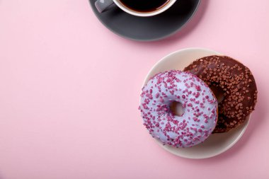 Çikolatalı donuts pembe arka plan üzerinde siyah kahve ile plaka üzerinde yakın çekim 