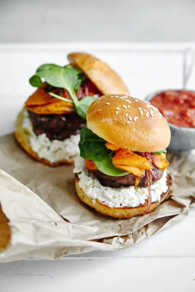 burgers with sauce in bowl on kitchen parchment paper sheets, close-up