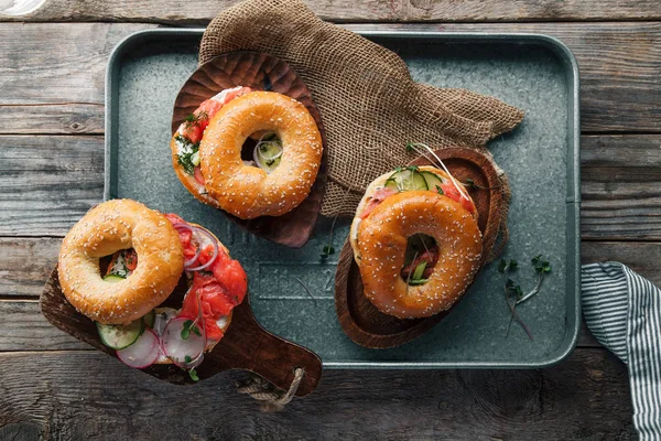 metallic tray with bagels and salmon fish with cream cheese and cucumber with fresh radish slices on rustic wooden background