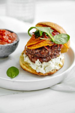 Beyaz seramik plaka burger ve ahşap masa, ıslak zeminde sos ile yakın çekim 