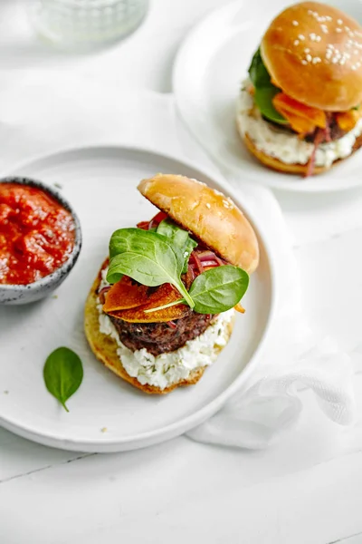 white ceramic plates with burgers and sauce in bowl on wooden table, close-up