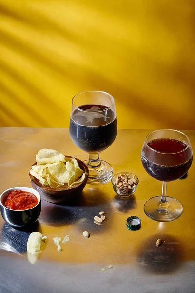 ale and stout beer in glasses with snacks and sauce in bowl on metallic and yellow background