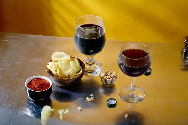 ale and stout beer in glasses with snacks and sauce in bowl on metallic and yellow background