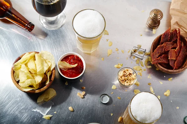 collection of snacks and glasses of cold beer with foam on sunlit metallic table