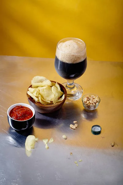 stout beer in glass with snacks and sauce in bowl on metallic and yellow background