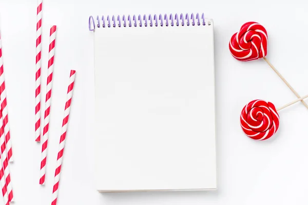 empty notebook with red and white party drinking straws with lollipops in round and heart form isolated on white background, close-up