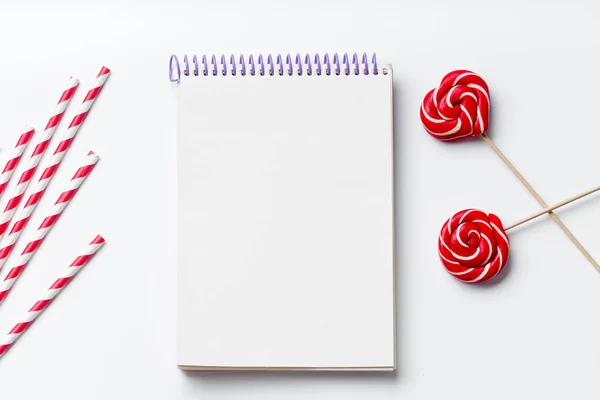 empty notebook with red and white party drinking straws with lollipops in round and heart form isolated on white background, close-up