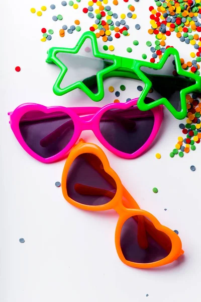 collection of childish sunglasses in bright colors and colorful sweet confetti topping isolated on white background, birthday party concept
