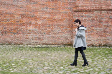 Açık portre karma yarış genç model siyah elbise ve tuğla duvar yanındaki yürüme gri ceket giymiş