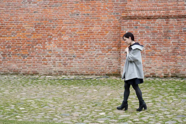 Açık portre karma yarış genç model siyah elbise ve tuğla duvar yanındaki yürüme gri ceket giymiş