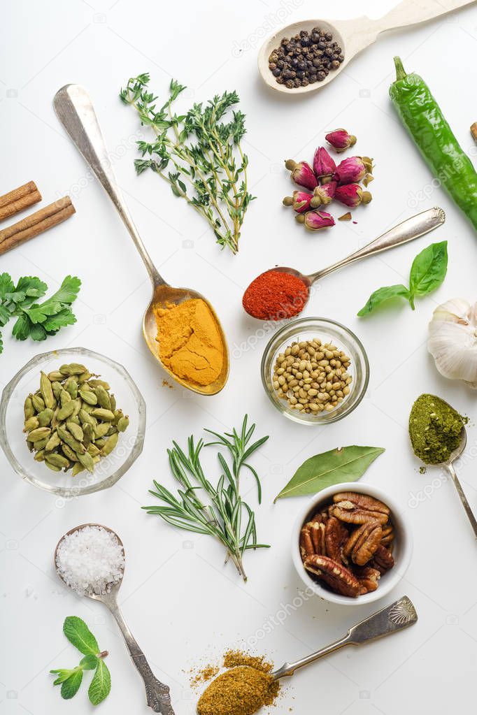 Fresh herbs and dried colorful spices in spoons and bowls arranged geometrically on white background