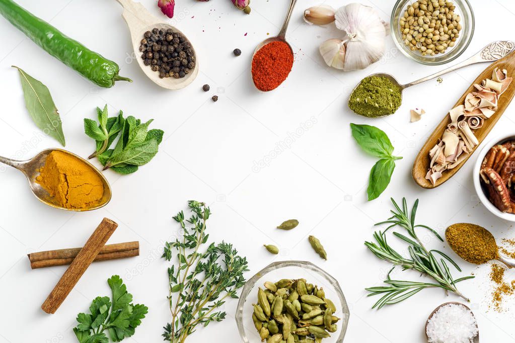 Fresh herbs and dried colorful spices in spoons and bowls arranged geometrically on white background 