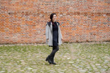 siyah elbise ve gri ceket tuğla duvar yanındaki yürüme karışık ırk genç modeli giymiş