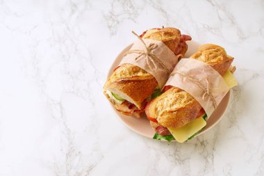 Pastırmalı ve peynirli baget sandviç ve mermer arka planda sebzeli marul.