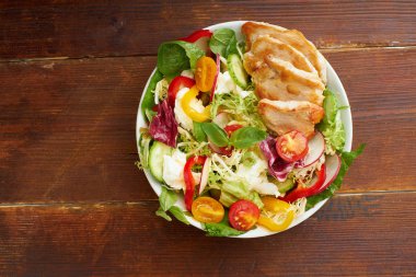 Healthy salad with tomatoes and chicken with bell peppers and radishes with mozzarella cheese on wooden background. Top view 