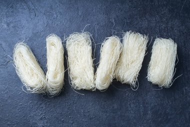  Koyu arkaplanda yuvalarda pişmemiş pirinç erişteleri. Asya mutfağının içeriği                  