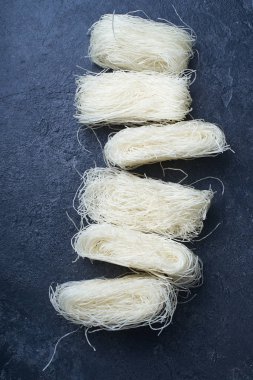  Koyu arkaplanda yuvalarda pişmemiş pirinç erişteleri. Asya mutfağının içeriği                  