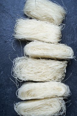  Koyu arkaplanda yuvalarda pişmemiş pirinç erişteleri. Asya mutfağının içeriği                  