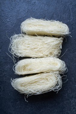  Koyu arkaplanda yuvalarda pişmemiş pirinç erişteleri. Asya mutfağının içeriği                  