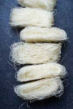  Koyu arkaplanda yuvalarda pişmemiş pirinç erişteleri. Asya mutfağının içeriği                  