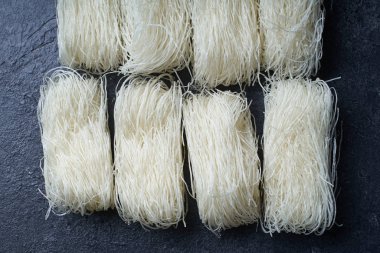  Koyu arkaplanda yuvalarda pişmemiş pirinç erişteleri. Asya mutfağının içeriği                  