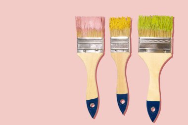 Pembe ve sarı renkli üç geniş fırça ve pastel arka planda yeşil boya.