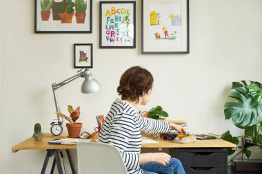 İş yerindeki kadın sanatçı evden çalışıyor. Kot pantolon ve çizgili gömlek giymiş genç bir kadın masada oturuyor ve bir illüstrasyon yaratıyor.. 